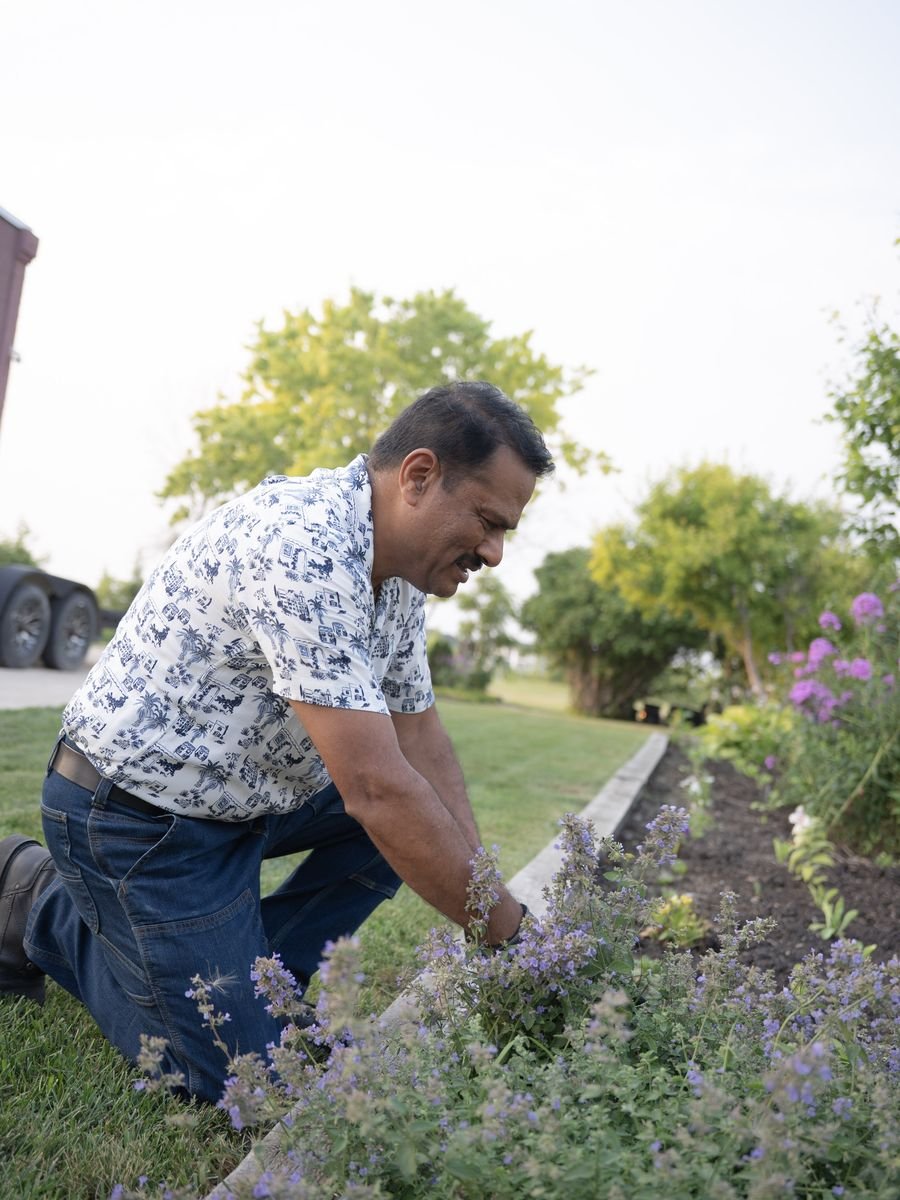 Jacky Maan kneeling to tend a flower bed in his yard